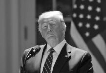 A man speaks at a podium with flag backdrop.