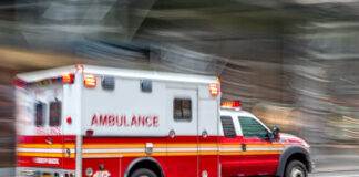 Red and white ambulance driving on a city street.