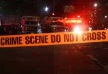 Crime scene tape with emergency vehicles in background.