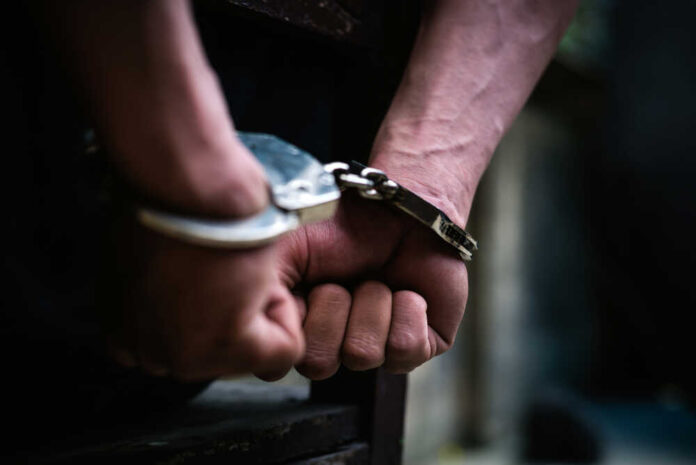 shutterstock_1338116366.jpg featured image Close-up of hands in handcuffs behind back.