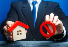 Businessman holding house model and prohibition sign