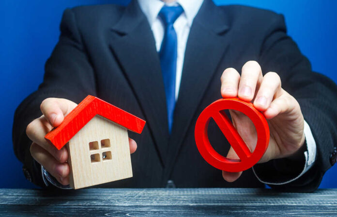 shutterstock_1679810578.jpg featured image Businessman holding house model and prohibition sign