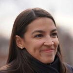 Alexandria Ocasio-Cortez, or AOC, smiling woman with long hair.