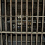 Empty, rusty barred jail cell with metal bunks.