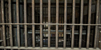 Empty, rusty barred jail cell with metal bunks.