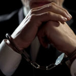Handcuffed person in suit, hands clasped together.