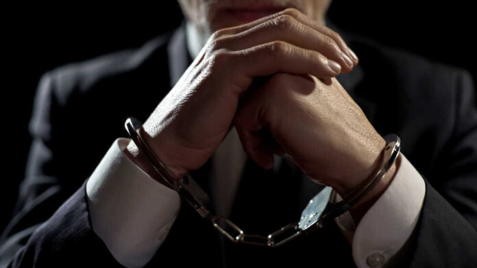 Handcuffed person in suit, hands clasped together.