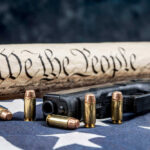 Gun, bullets, Constitution scroll on American flag.
