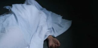 Hand emerging from under white sheet on dark surface.