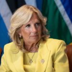 Insider ACCUSES Jill Biden of ELDER ABUSE! Jill Biden in a yellow blazer sitting, colorful flags behind.