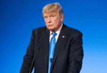 Man in suit with blue background speaking at podium