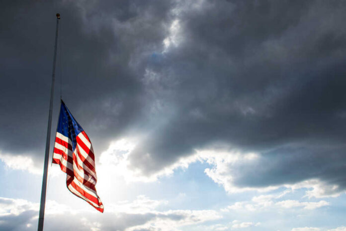 USA flag at half-mast under cloudy sky