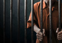 Man in orange prison uniform behind jail bars
