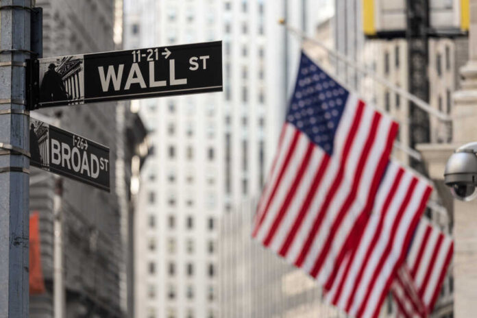 Street signs for Wall Street and Broad Street with American flags in the background