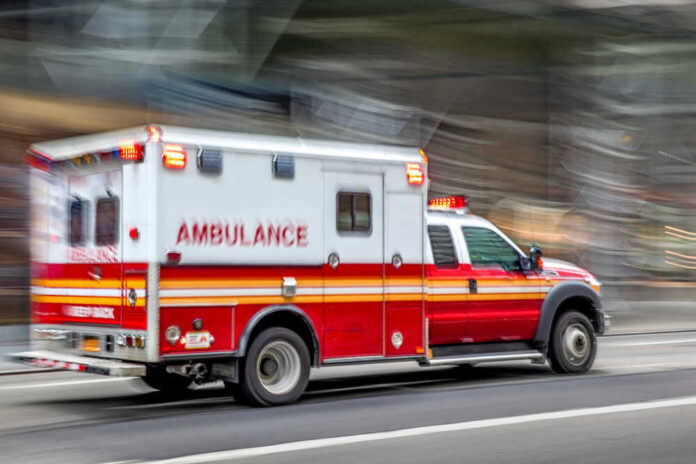 Red and white ambulance driving on a city street.