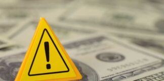 A yellow warning sign placed on a pile of dollar bills