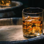 Glass of whiskey with ice on a wooden barrel.