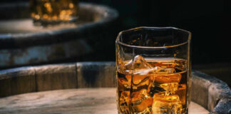 Glass of whiskey with ice on a wooden barrel.