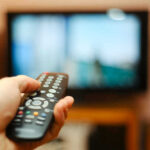 Hand holding a remote control towards a TV screen.