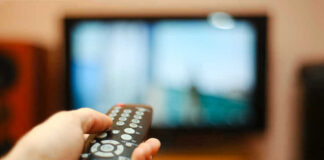 Hand holding a remote control towards a TV screen.
