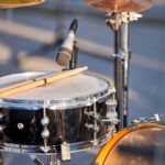 Close-up of a snare drum with drumsticks resting on it and a microphone nearby