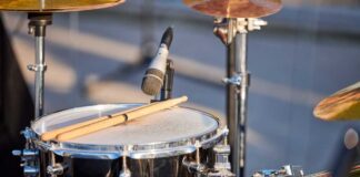 Close-up of a snare drum with drumsticks resting on it and a microphone nearby
