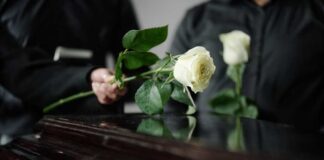 Two individuals placing white roses on a coffin during a funeral