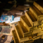Stack of gold bars next to scattered banknotes and coins