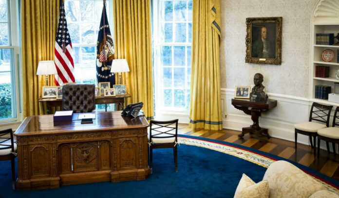 Presidential office with desk, flags, and portraits.