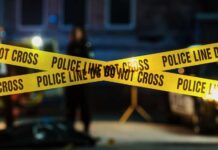 Teen Gunman Dead After Shooting Teacher Police tape marking a crime scene with blurred figures in the background