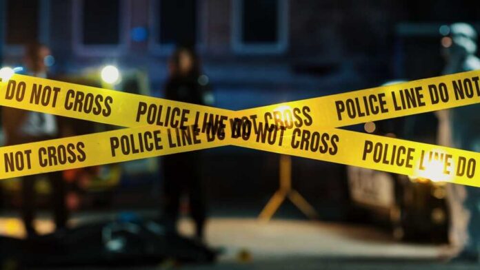 shutterstock_2230640037.jpg Police tape marking a crime scene with blurred figures in the background
