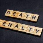 Wooden letter tiles spelling DEATH PENALTY on a dark background
