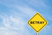 A yellow warning sign with the word 'BETRAY' against a blue sky