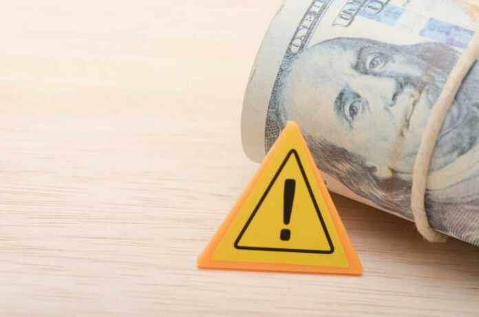 A roll of cash next to a warning sign on a wooden surface