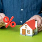 Person holding a percentage symbol above a model house