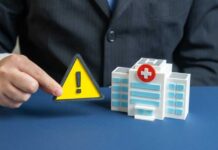 A business professional holding a warning sign next to a model of a hospital