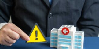 A business professional holding a warning sign next to a model of a hospital