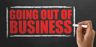 A hand writing 'GOING OUT OF BUSINESS' on a chalkboard