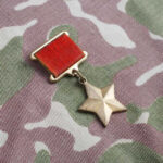 A military medal featuring a red ribbon and a star on a camouflage fabric