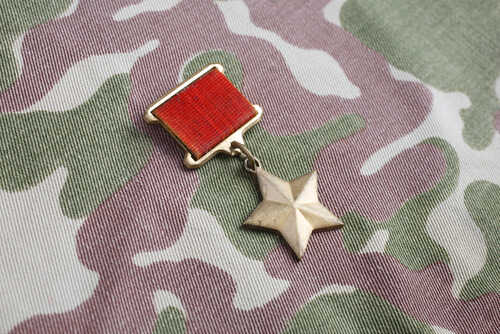 shutterstock_691157851 (1).jpg A military medal featuring a red ribbon and a star on a camouflage fabric