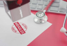 A stamp marking 'MEASLES ALERT' on a piece of paper next to a stethoscope and keyboard