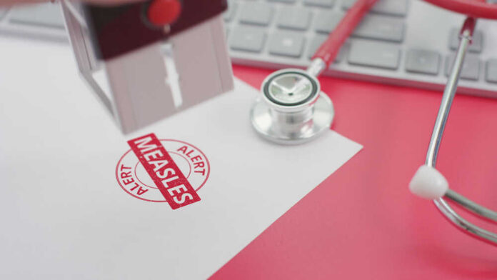 A stamp marking 'MEASLES ALERT' on a piece of paper next to a stethoscope and keyboard