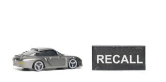 A miniature gray sports car next to a black sign that reads 'RECALL'