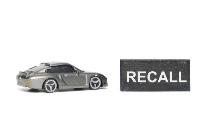 shutterstock_2346652001.jpg A miniature gray sports car next to a black sign that reads 'RECALL'