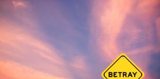 A yellow warning sign with the word 'BETRAY' against a colorful sunset sky