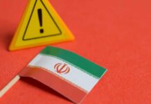 Iran War SLAMS E-Commerce Costs Iranian flag next to a caution sign on a red background
