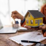 Person holding a small yellow model house while holding keys