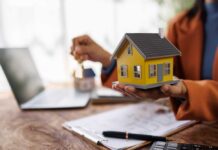 Person holding a small yellow model house while holding keys