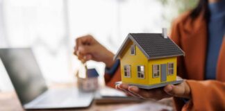 Person holding a small yellow model house while holding keys