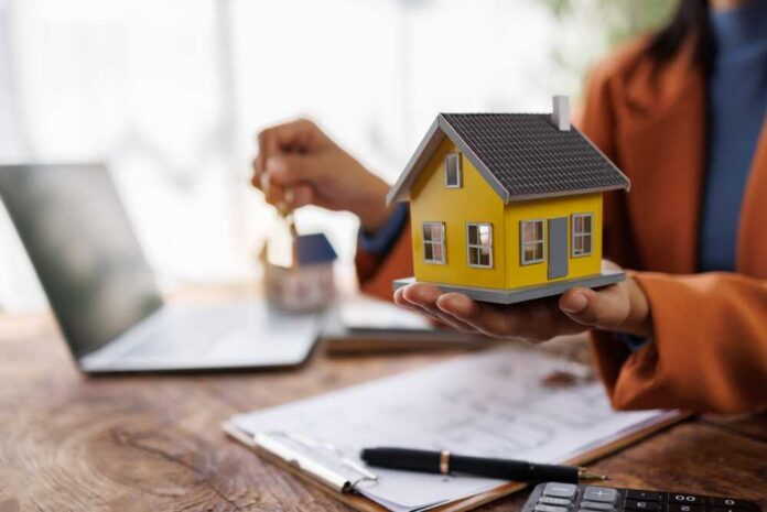 Person holding a small yellow model house while holding keys
